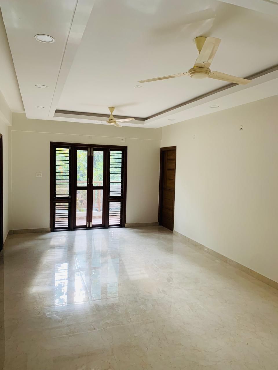 Bright living hall with dark-wood louvred balcony doors and false ceiling