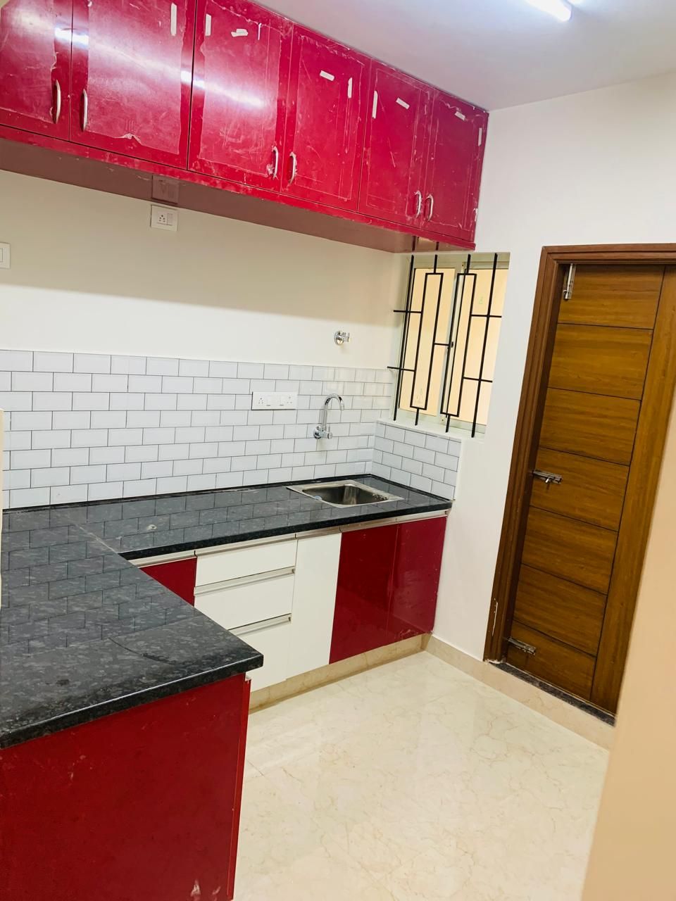 Red high-gloss modular kitchen with black granite counter and subway tile
